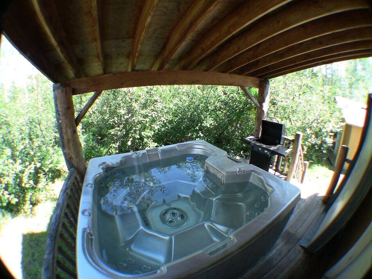 A hot tub with a wooden deck and a view of a lush garden.