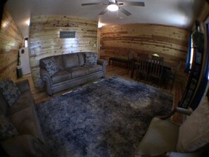 A room with a wooden wall, a sofa, a rug, and a ceiling fan. - Aspen Hideaway +Hot Tub+15 min from Yellowstone (Island Park)