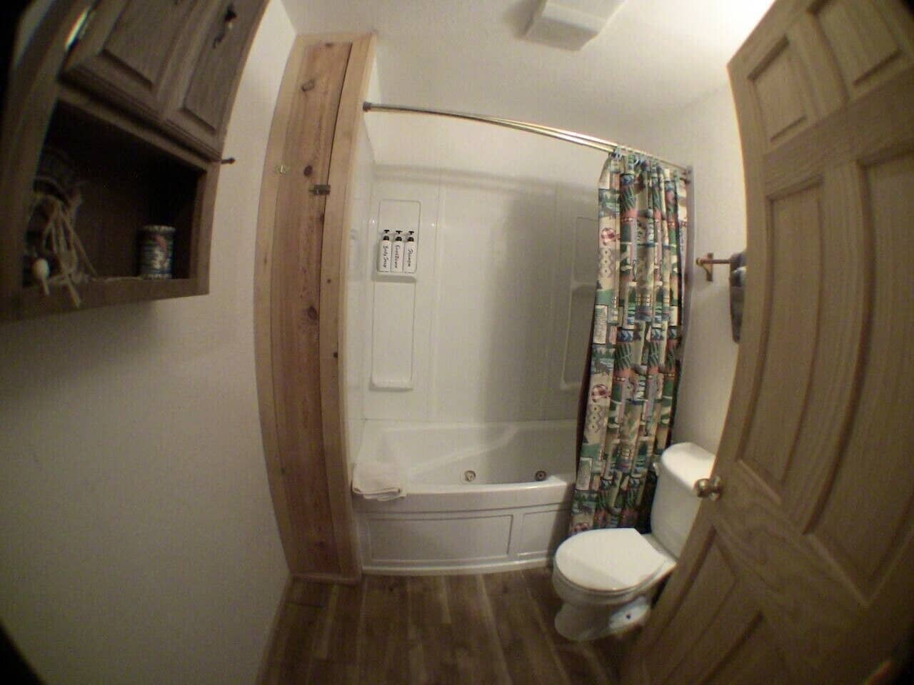 A bathroom with a shower, toilet, and wooden cabinets.
