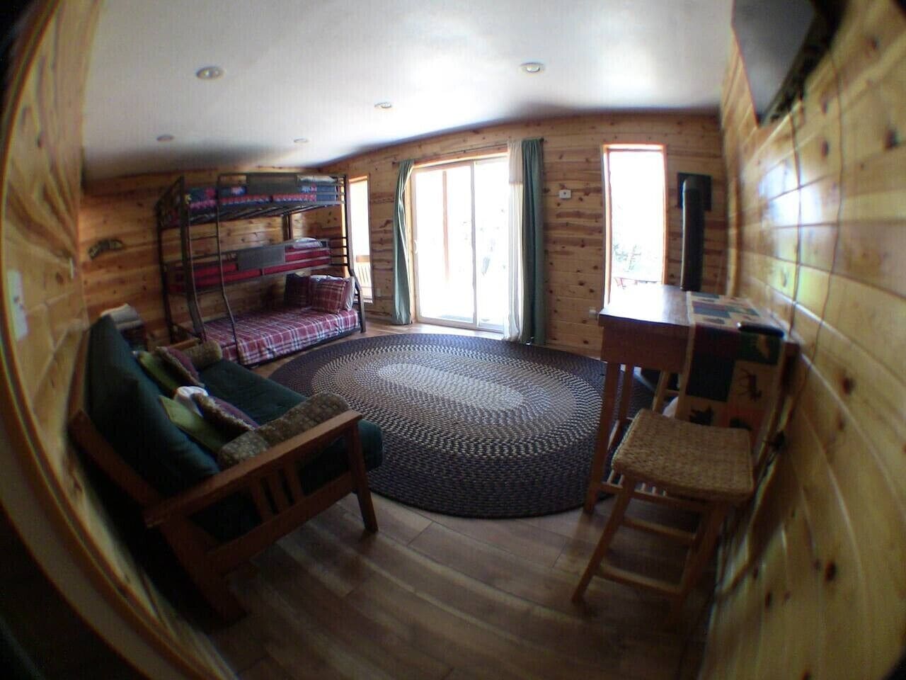 A cabin interior with a bunk bed, a round rug, a wooden table, and a chair.