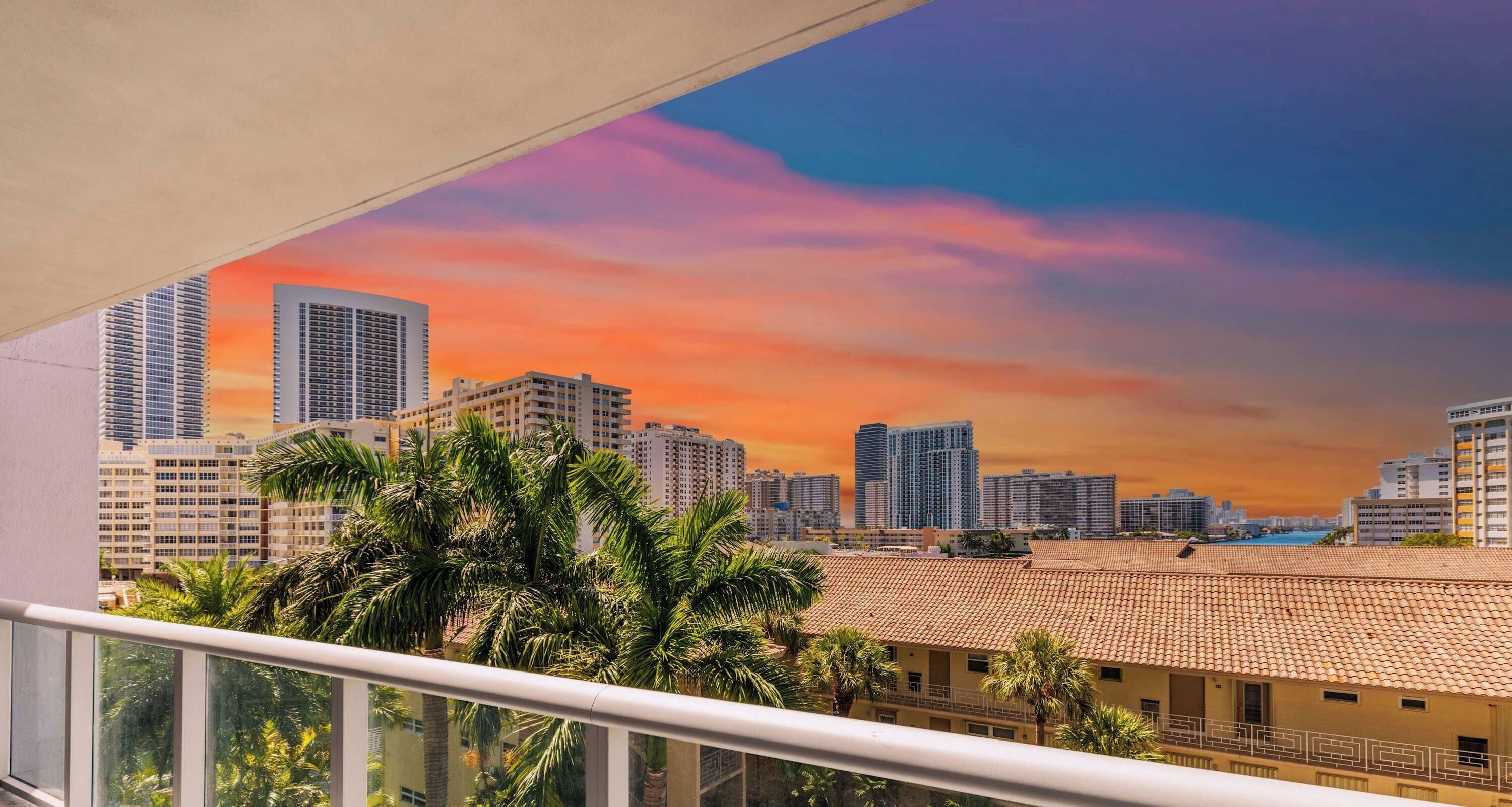 A balcony with a view of a cityscape during sunset, featuring high-rise buildings and palm trees.