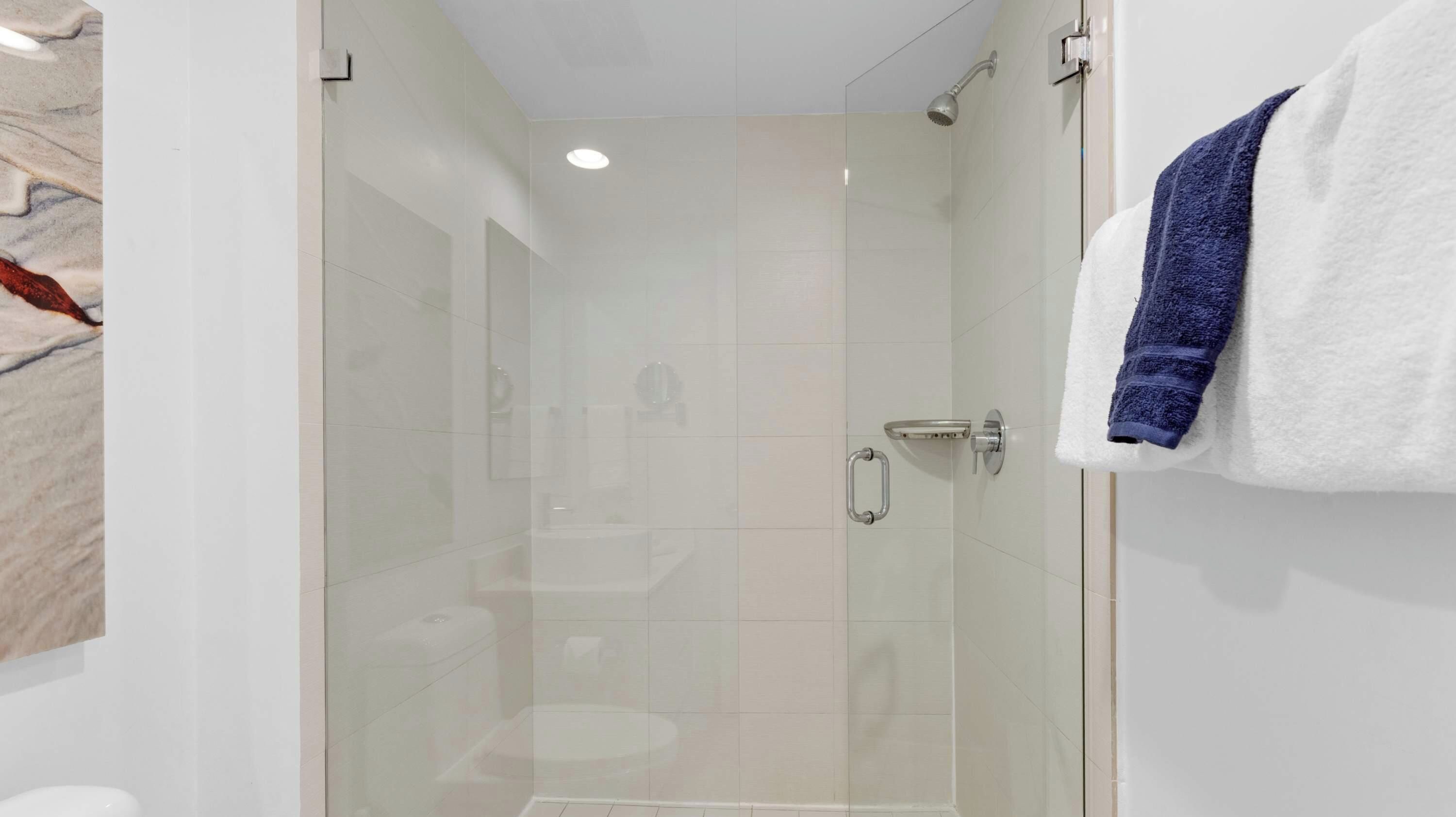 A modern bathroom with a glass-enclosed shower, a white toilet, and a towel rack with a blue towel.