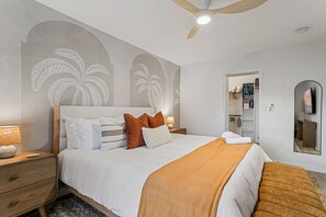 Een slaapkamer met een bed, nachtkastjes, een plafondventilator, een aan de muur bevestigde televisie en een deur die naar een badkamer leidt.