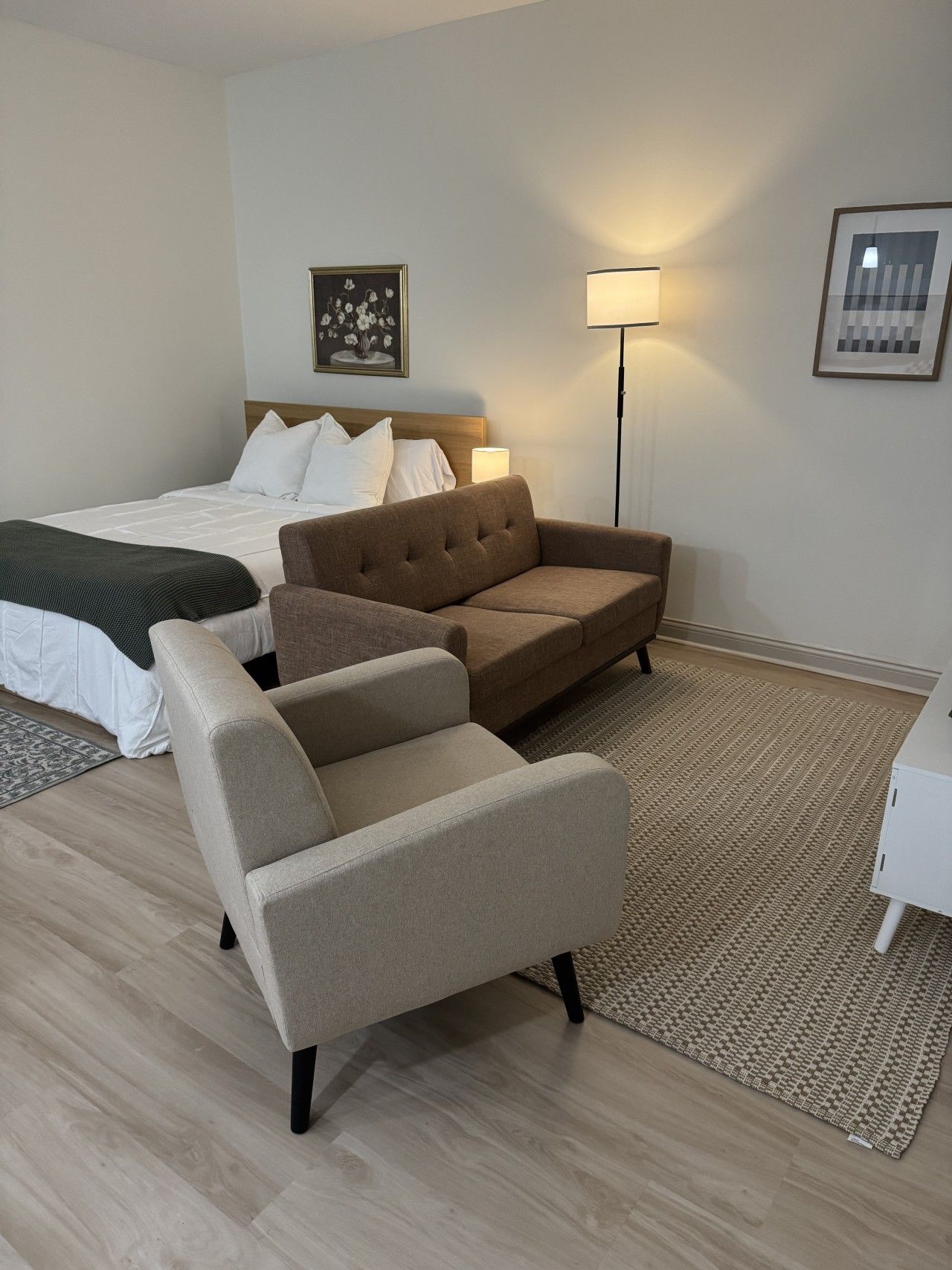 Een hotelkamer met een bed, twee banken, een vloerlamp en een vloerkleed.