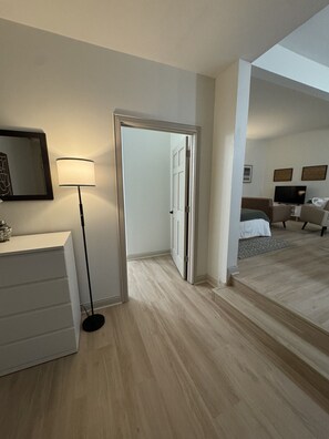 A hotel room with a white dresser, a floor lamp, and a bed with a grey headboard. - 103 Studio Apt, quiet, cozy, medium & Long Stays! (Indianapolis)