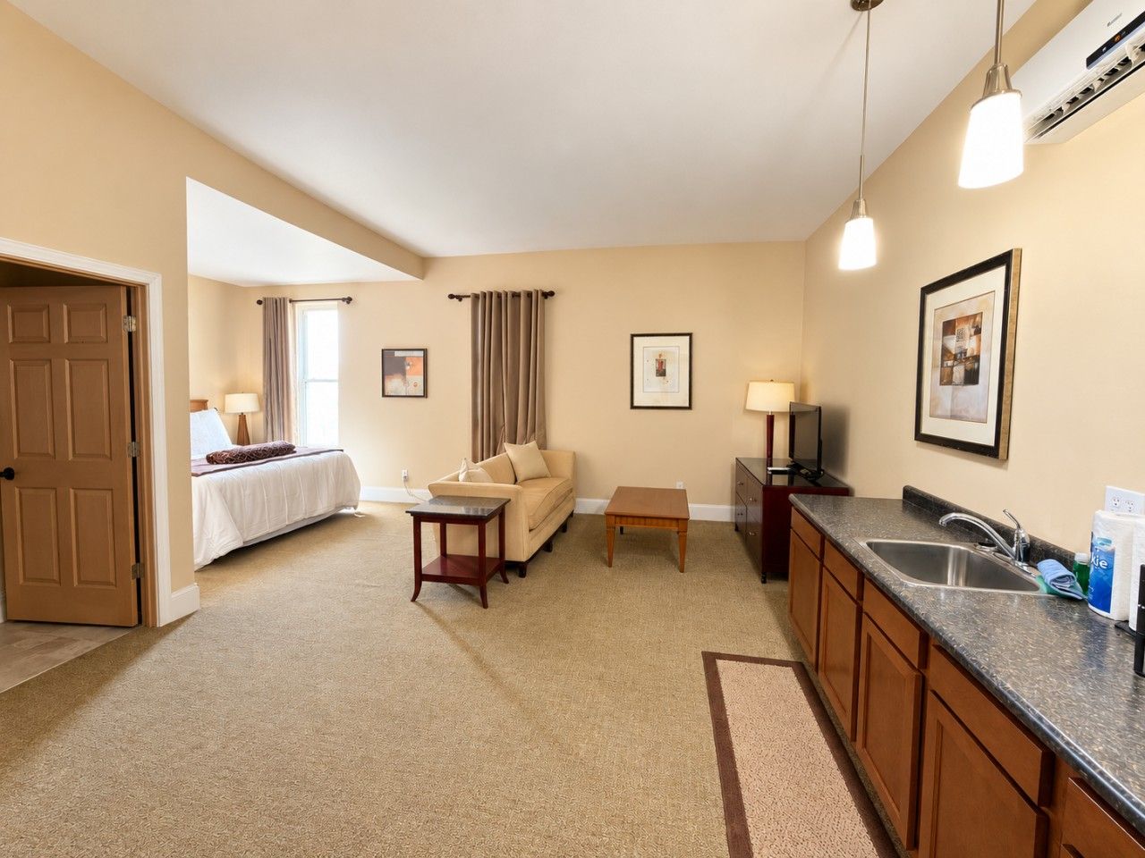 Une chambre d’hôtel comprenant un lit, un canapé, une petite table, un coin cuisine avec un évier et une porte donnant sur une autre pièce.