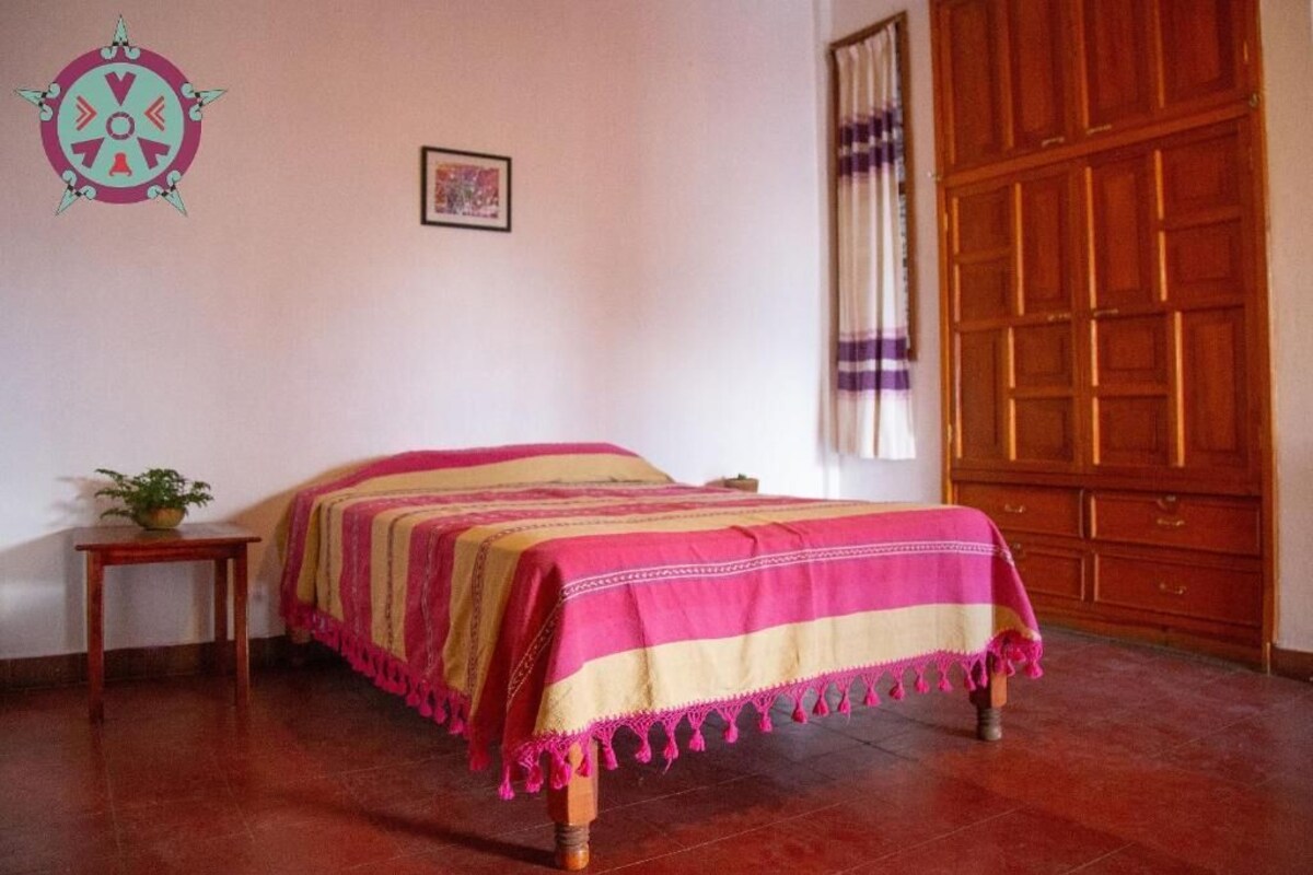 A bedroom with a bed, a wooden wardrobe, a small table with a plant, and a wall decoration.