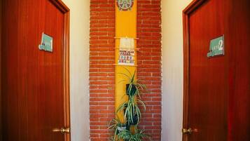 Un pasillo con dos puertas de madera, cada una con un número de habitación. Una columna amarilla vertical con un reloj y una pequeña señal está entre las puertas.