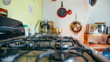 Una cocina con estufa a gas, ollas, microondas y un estante de madera.