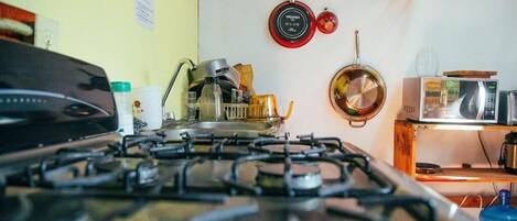 A kitchen with a gas stove, pots, a microwave, and a wooden shelf.