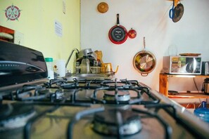 Eine Küche mit einem Gaskochfeld, Töpfen, einer Mikrowelle und einem Holzregal.
