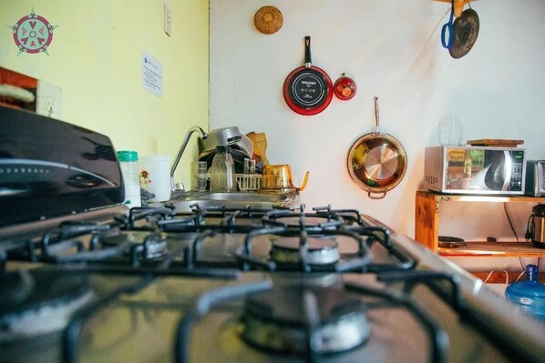 A kitchen with a gas stove, pots, a microwave, and a wooden shelf.