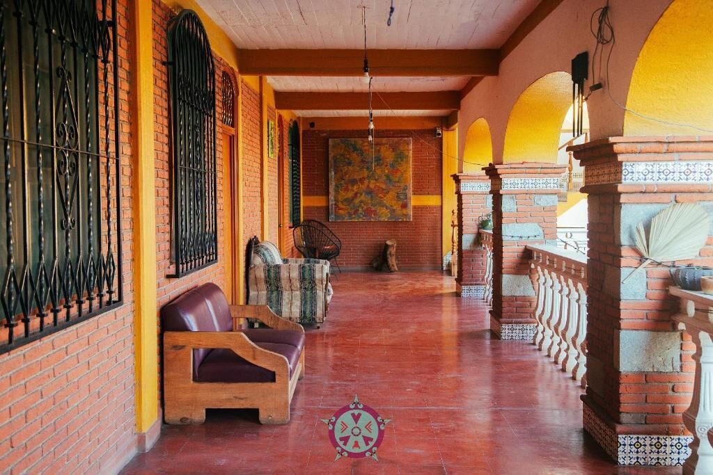 A corridor with brick walls, a wooden bench, a patterned rug, and a decorative wall hanging.