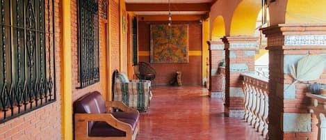 A corridor with brick walls, a wooden bench, a patterned rug, and a decorative wall hanging.
