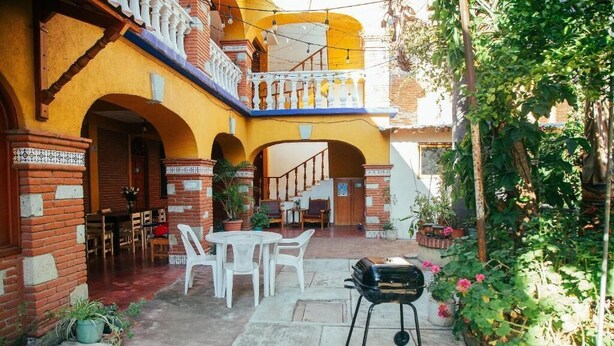 Un cortile con una griglia barbecue, sedie bianche e piante in vaso.