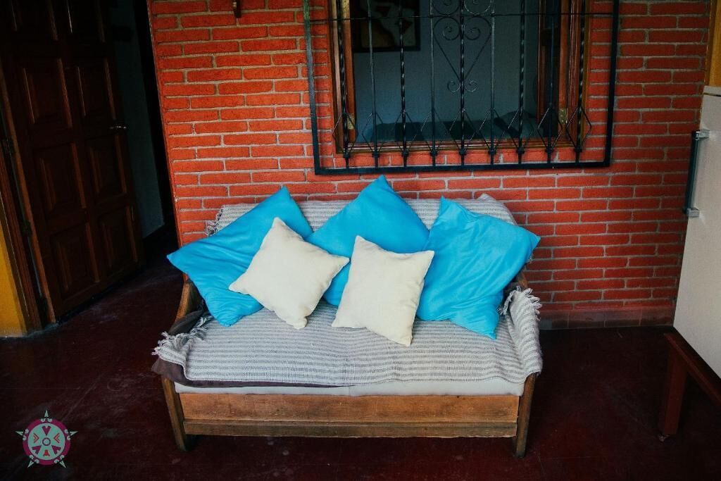 Una cama con una colcha a rayas y almohadas azules y blancas, frente a una pared de ladrillo con una ventana y una puerta.