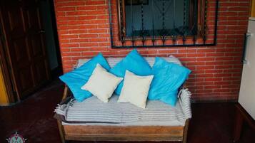 Una cama con una colcha a rayas y almohadas azules y blancas, frente a una pared de ladrillo con una ventana y una puerta.