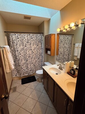 Un bagno con tenda da doccia, water, lavabo e mobiletto.