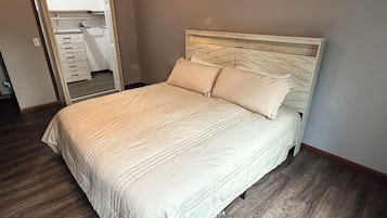 A bedroom with a bed, wooden flooring, and a door leading to another room.