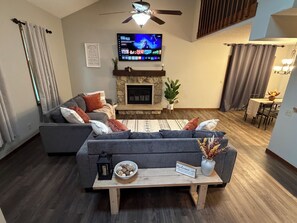 Una sala de estar con un sofá, una mesa de centro con un letrero de bienvenida, una chimenea y un televisor montado en la pared.