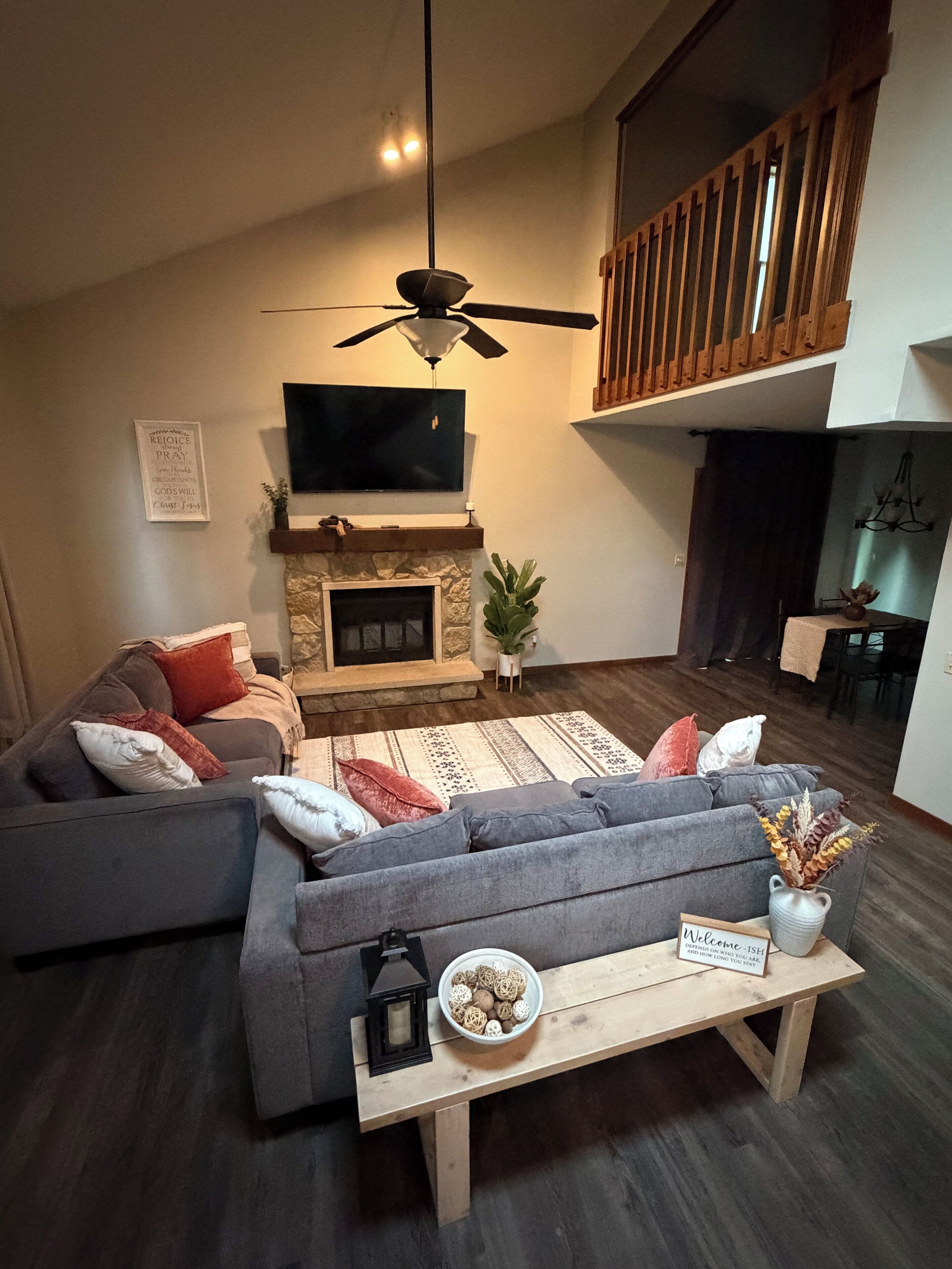 A modern living room with a fireplace, a ceiling fan, and a view of the upper floor.