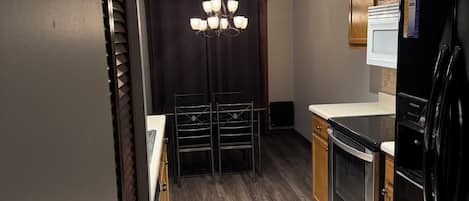 A kitchen with a black refrigerator, a microwave, and a stove. There is a chandelier hanging from the ceiling.