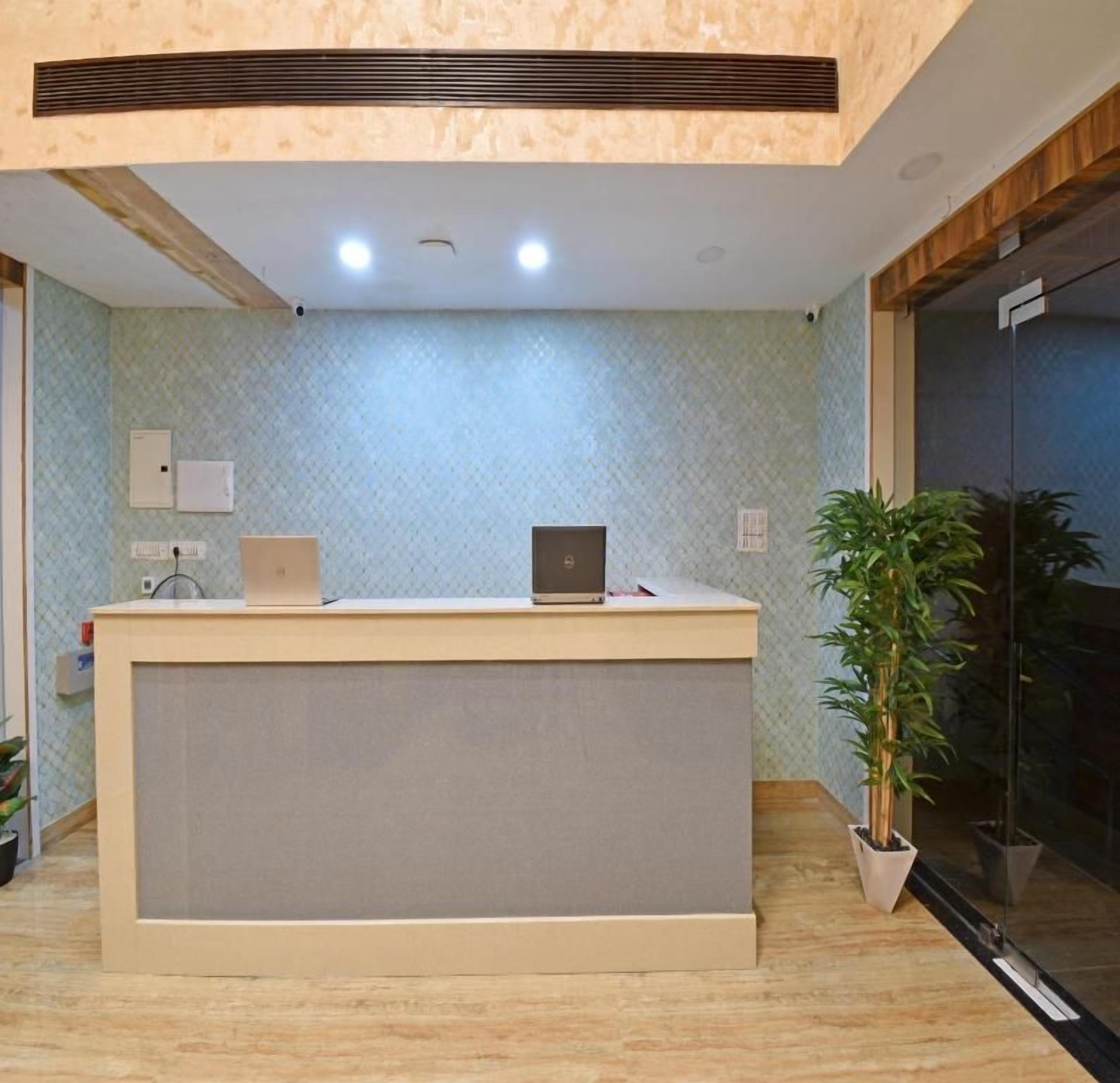 A reception desk with a laptop, a potted plant, and a wall-mounted light fixture.