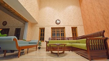 Une pièce spacieuse avec un plafond haut, un ensemble de meubles de salon en bois, une petite table ronde et une horloge au mur.