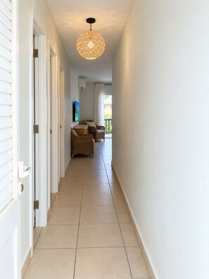 Un couloir avec un luminaire au plafond, une porte et une vue sur un balcon aménagé avec du mobilier d’extérieur.