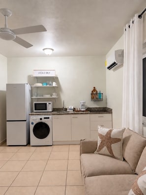 Ein kompakter Wohnbereich mit Küchenzeile, Deckenventilator, Waschmaschine und einer Couch mit einem Seesternkissen.