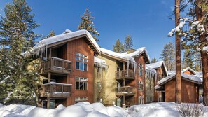 Un chalet à plusieurs étages doté de balcons, entouré d’arbres couverts de neige.