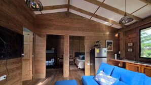 Ein gemütliches Blockhauss-Interieur mit Holzvertäfelung, einem blauen Sofa, einer Küchenzeile und einem großen Fenster.