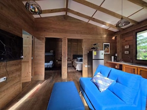 A cozy cabin interior with a wooden interior, a blue sofa, a kitchen area, and a large window.