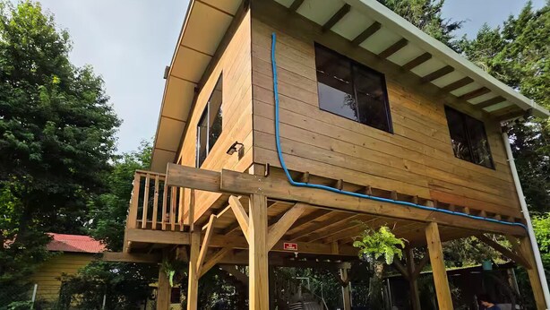 Ein zweistöckiges Holzhaus mit Balkon, überdachter Terrasse und Blumentopf.