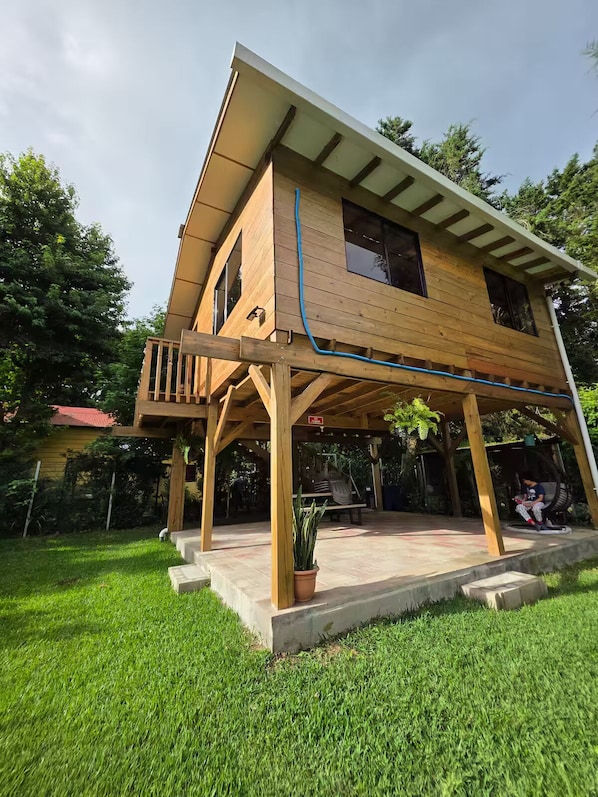 A two-story wooden house with a balcony, a covered patio, and a potted plant.