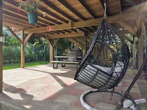 A covered outdoor area with a hanging chair, a picnic table, and a hanging planter.