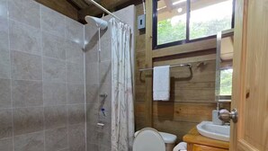 Ein kleines Badezimmer mit Dusche, Toilette und Waschbecken, ausgestattet mit Holzbalken und einem Fenster.