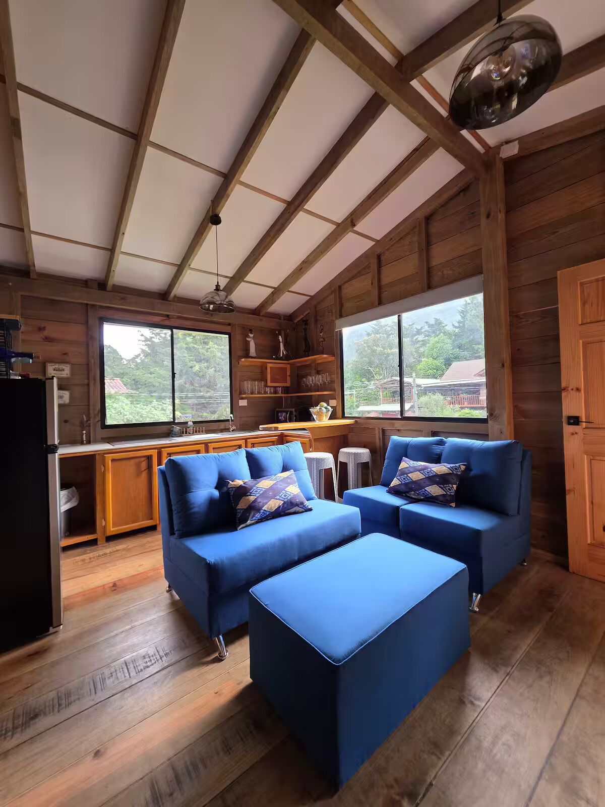 Interior acogedor de una cabaña con techo de madera, una kitchenette y una zona de estar con sofás azules.
