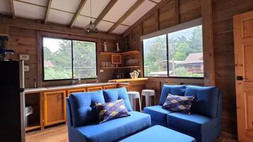 Interior acogedor de una cabaña con techo de madera, una kitchenette y una zona de estar con sofás azules.