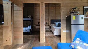 Ein Holzblockhaus-Interieur mit einem Etagenbett, einem Schreibtisch, einem Kühlschrank und einem blauen Sofa.
