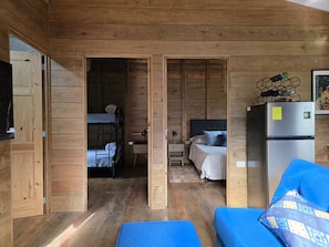 A wooden cabin interior with a bunk bed, a desk, a refrigerator, and a blue sofa.