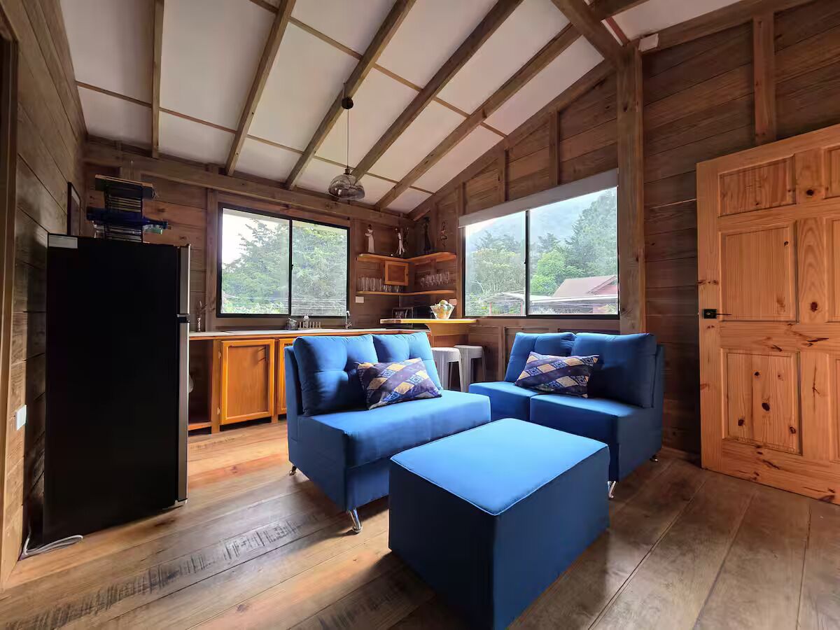Ein gemütliches Blockhaus-Interieur mit Holzbalkendecke, einer Küchenzeile und einer Sitzecke mit blauen Sofas und Poufs.