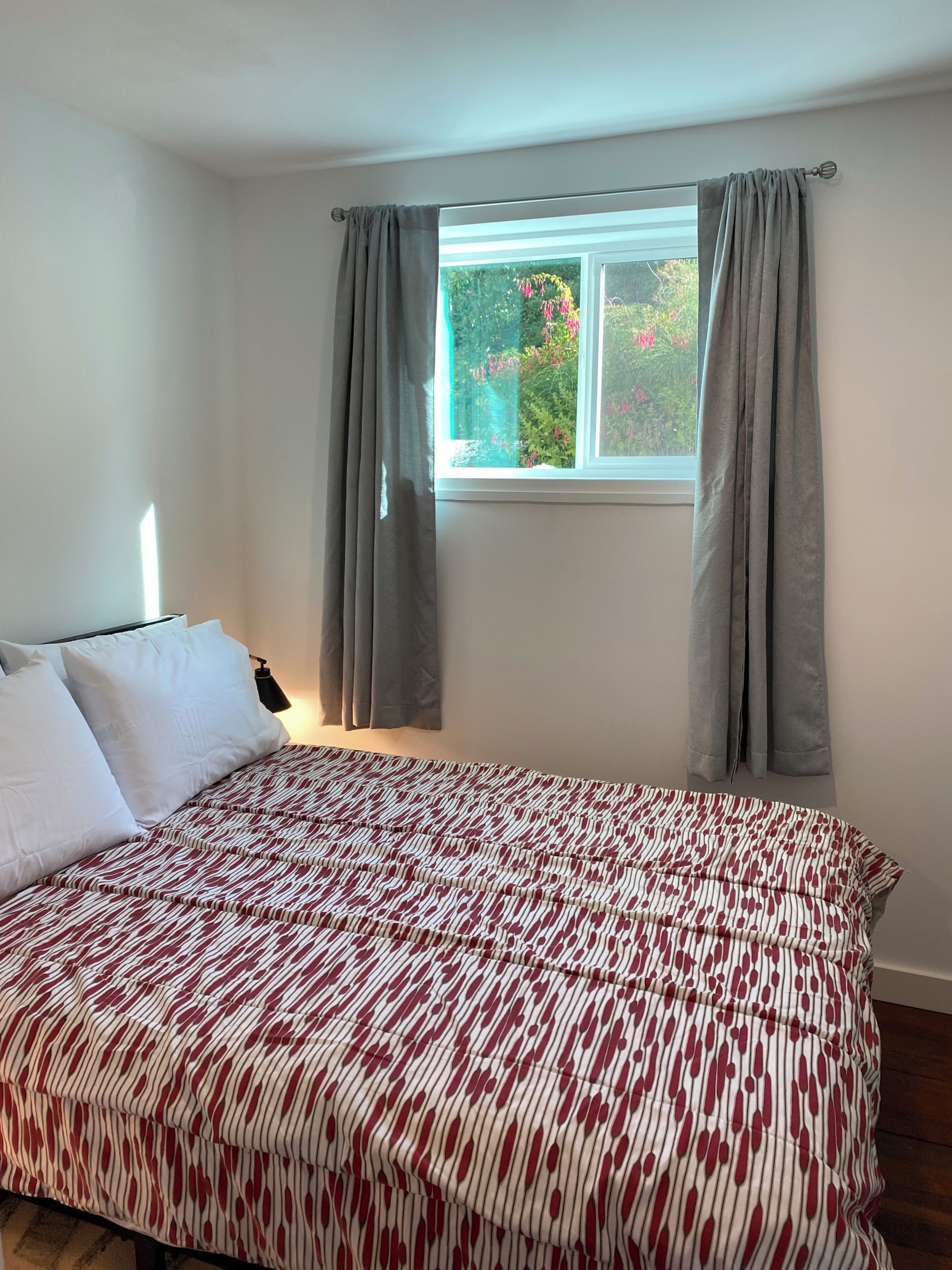 A bedroom with a bed, curtains, a window, and a view of greenery outside.
