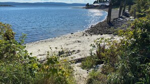 Ein Strand mit felsigem Ufer, blauem Himmel und Bergen in der Ferne.
