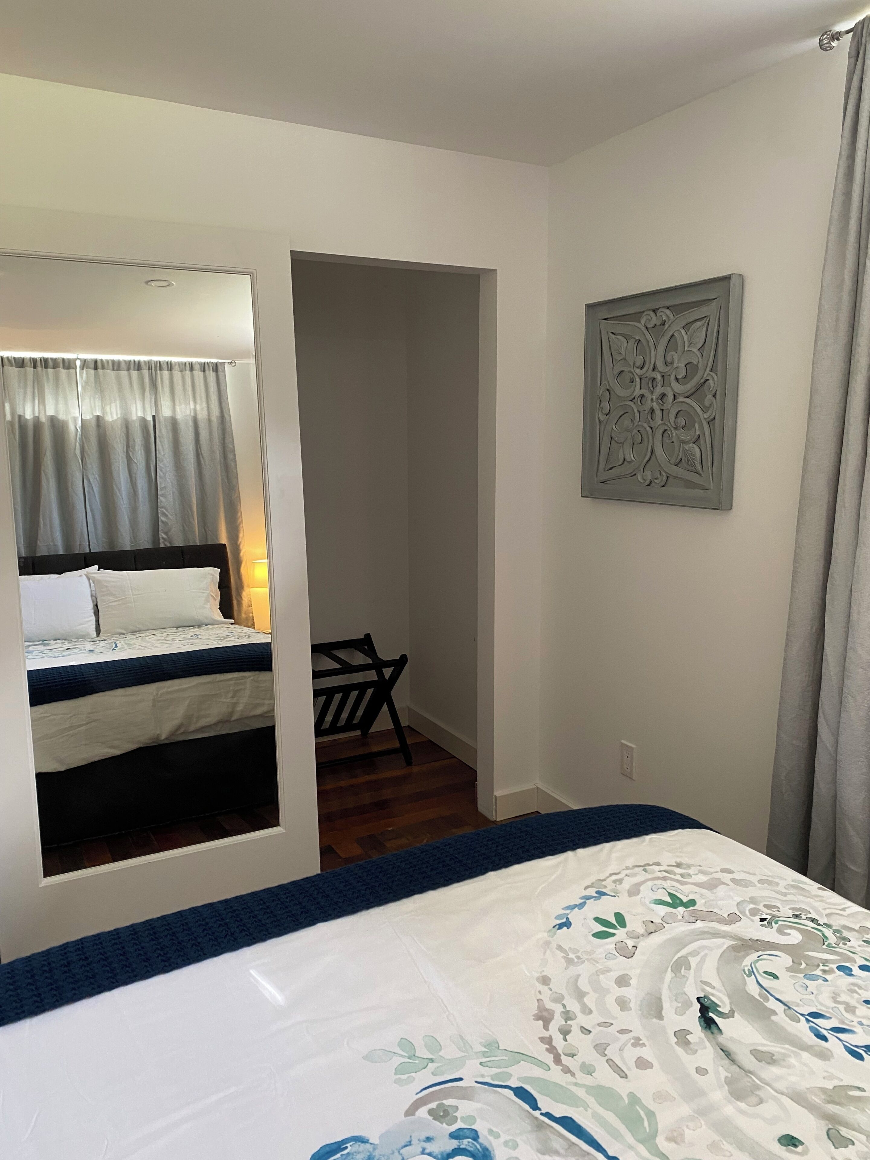 A bedroom with a bed, a chair, a door leading to another room, and a wall-mounted decorative piece.