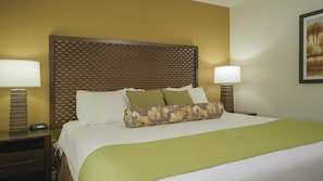 Une chambre d’hôtel avec un grand lit, deux lampes de chevet, une tête de lit à motifs et un tableau au mur.