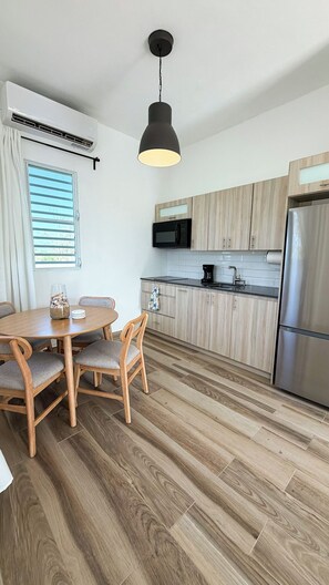 A modern kitchen with wooden cabinets, a stainless steel refrigerator, and a dining area with a wooden table and chairs. - Beach Lote Villas - Villa 2 +Pool- Islote (Arecibo)
