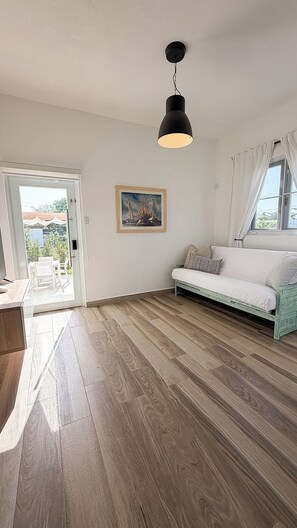 Une pièce avec un plancher en bois, un canapé blanc, un tableau au mur et un luminaire au plafond.