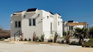 Een modern huis met twee verdiepingen, een plat dak, witte buitenmuren en een klein portaaltje met een pergola.