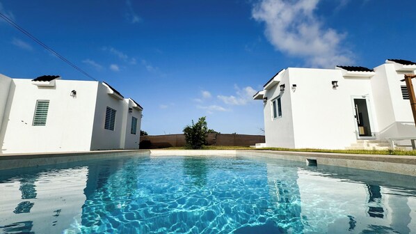 Une piscine à l’eau d’un bleu cristallin, entourée de bâtiments blancs dotés de fenêtres et de portes.
